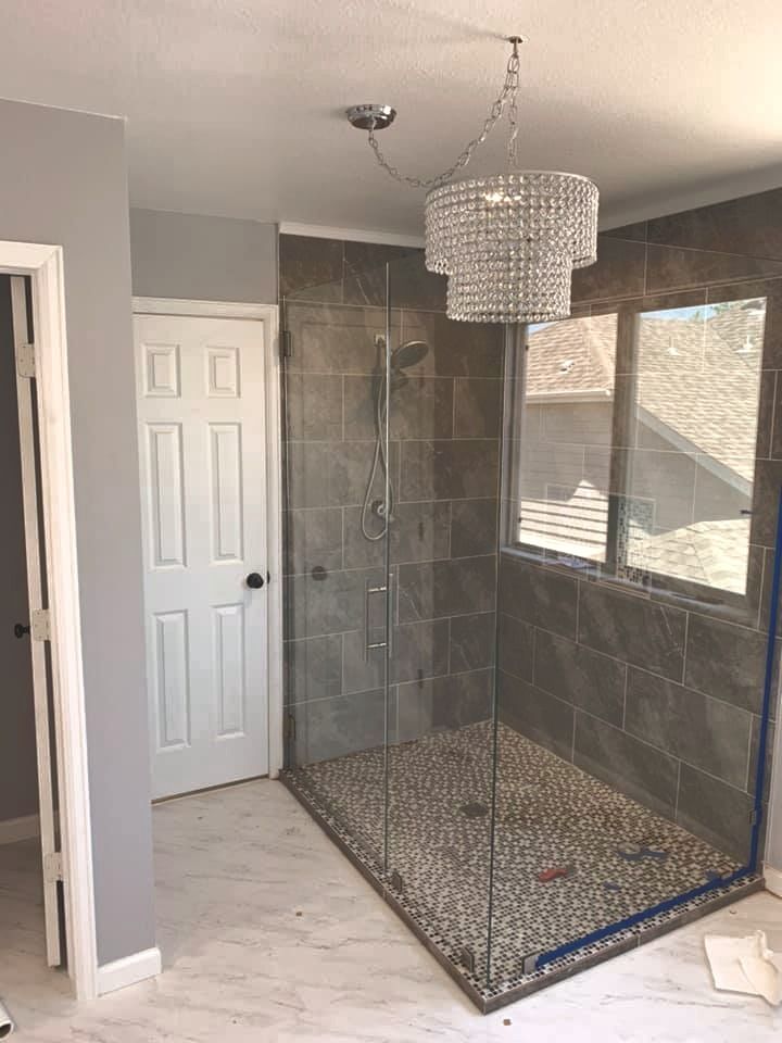 Frameless glass shower enclosure with a chrome handle, stone tile, and a window inside the stall